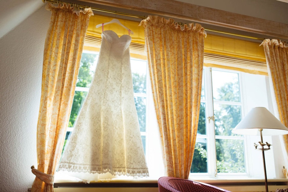 Hochzeit im kleinen Kreis das Hochzeitskleid aus Spitze hängt im Fenster